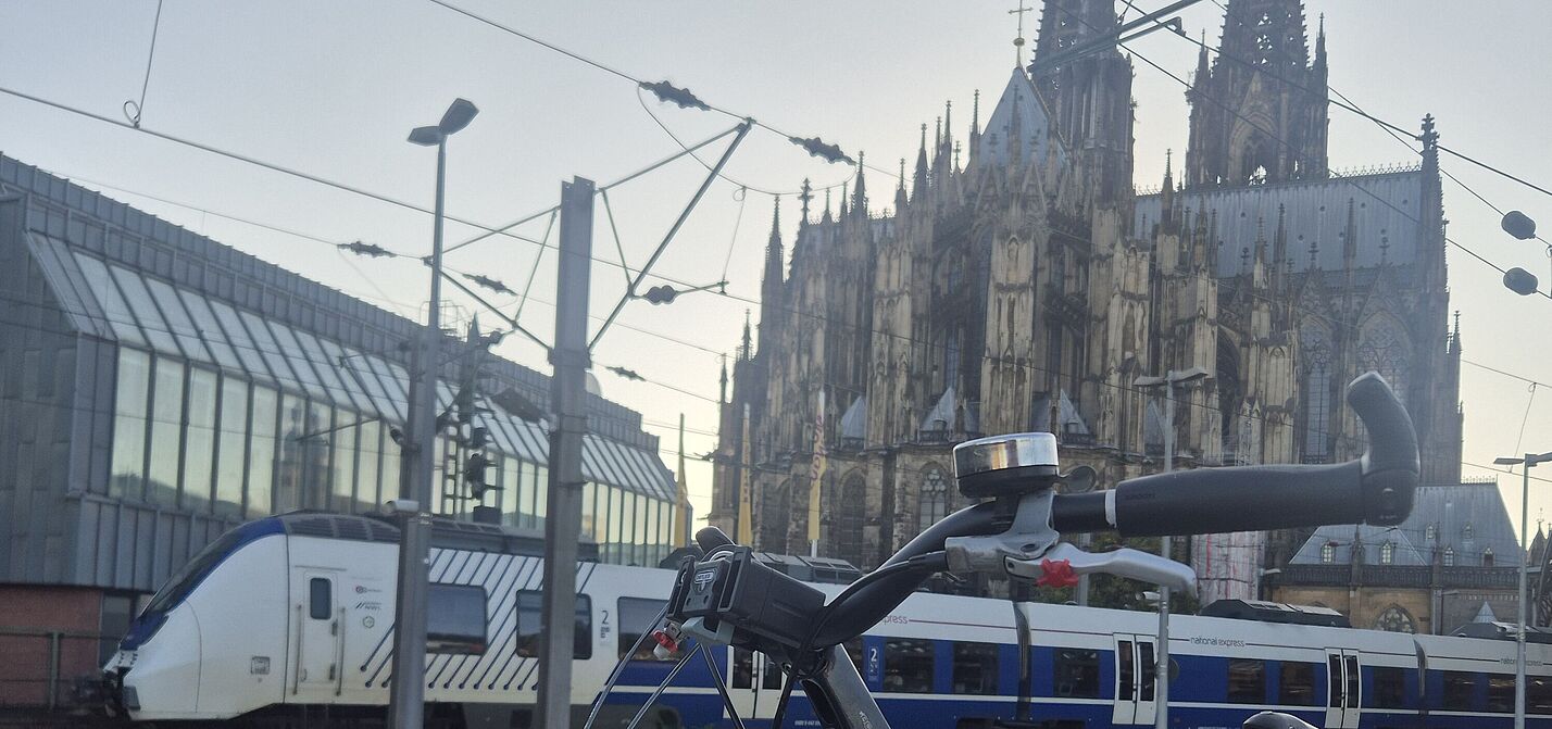 2025-09_Exkursion_Mobilitaet_Dortmund__ADFC_NRW Nahverkehrszug am Hauptbahnhof in Köln. Fahrrad auf Bahnsteig. Dom im Hintergrund.