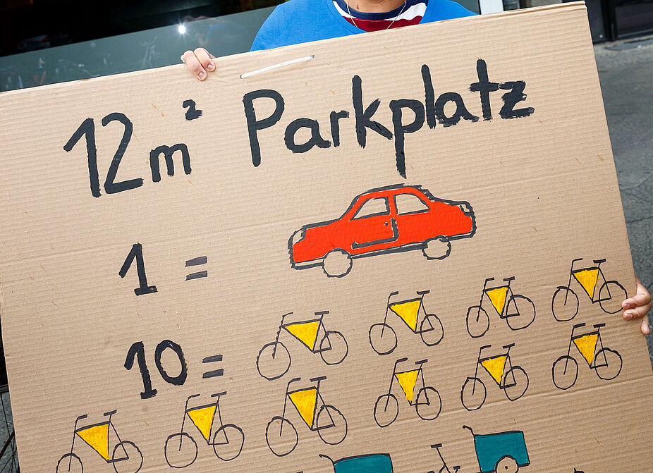 Demo #MehrPlatzFürsRad Frau hält Plakat mit Aufschrift: Ein Autoparkplatz = 12 Fahrräder = 4 Lastenräder